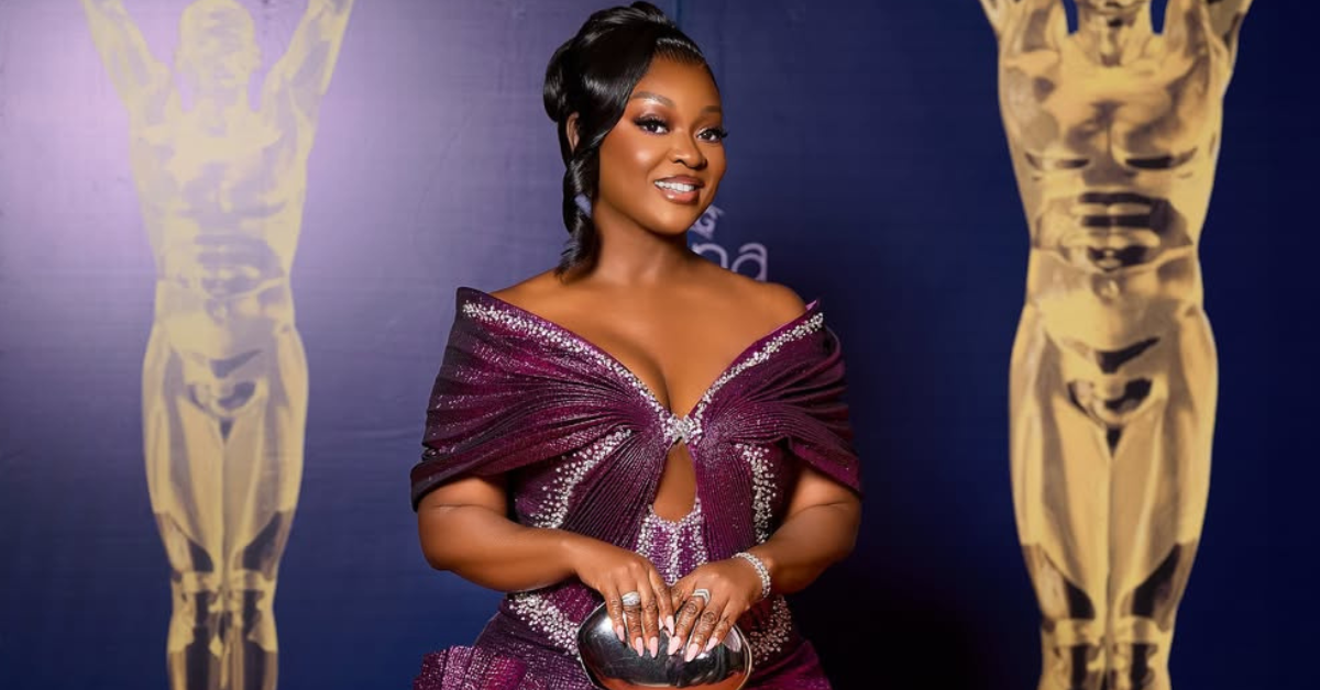 Jackie Appiah wearing a sculptural metallic magenta-purple gown with origami-inspired pleats and rhinestone detailing at the 2026 Ghana Movie Awards red carpet in Accra.